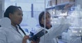 Pointing team in white coats annotating glass panel in lab, holding tablet and markers with charts Royalty Free Stock Photo