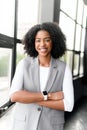 A poised African-American businesswoman with a cheerful demeanor stands arms crossed in a modern office