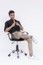 A poised young Filipino man dressed in smart casual clothes seated on an office chair, isolated on a white background