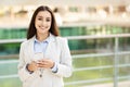 A poised young woman in a business suit smiles warmly while holding and looking at her smartphone