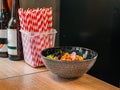Poke bowl on black plate and white-red plastic tubes for milkshakes, cocktails stands on counter next to beer bottles, on wooden t Royalty Free Stock Photo