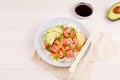 Poke bowl with salmon, rice, avocado, micro greens, pepper and soy sauce on white wooden background. Royalty Free Stock Photo