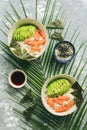 Poke bowl with salmon rice and vegetables on grey background with palm leaves. Traditional Hawaiian raw fish salad. Top view Royalty Free Stock Photo