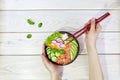 Poke bowl with salmon, rice and vegetables. Women's hands hold chopsticks and a bowl with hawaiian ahi Royalty Free Stock Photo