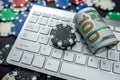 Poker chips and wads of dollars on a laptop keyboard scattered over a plain background. Royalty Free Stock Photo