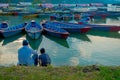 Pokhara, Nepal - September 04, 2017: Father and son sitting in the lakeshore enjoying the view of the boats in the lake