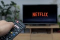 Person holding a TV remote controller displaying the Netflix logo with the Netflix platform visible on the TV screen Royalty Free Stock Photo