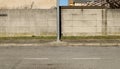 Pole on cement sidewalk with concrete wall, a brick wall and residential buildings on behind. Urban street in front. Royalty Free Stock Photo