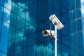 Pole with two white video surveillance cameras at big office glass building background