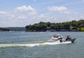 Police boat zipping through the waters with homes and boat docks on the shore and other boats and PWCs farther out on the lake - G