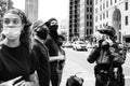 Police officer in body armor stands in front of a crowd of protestors and puts on a respirator