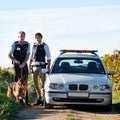 Policeman, dog and car in field to search at crime scene or robbery for safety, law enforcement and evidence. Detective