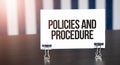 Policies and Procedure sign on paper on dark desk in sunlight. Blue and white background