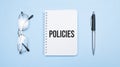 POLICIES words in white notepad, pen and glasses on blue background. Concept