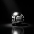 A polished chrome sphere sits on a dark reflective surface, casting a soft Royalty Free Stock Photo