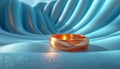 A polished copper ring rests on a silky, blue draped fabric, reflecting a soft glow