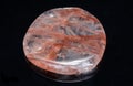 Polished quartz flat palm stone with red hematite inclusions from Madagascar isolated on black background Royalty Free Stock Photo