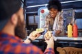 Polite afro-american female employee holding, giving, two sandwiches to a beardy caucasian customer. fast food service