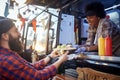 Polite female employee holding, giving, two sandwiches to a satisfied beardy customer