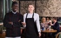 Polite waitress standing in restaurant hall with cheerful African American chef, meeting guests Royalty Free Stock Photo