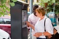 Polite intelligent African man helping middle aged woman to buy ticket in parking meter on summer city street Royalty Free Stock Photo