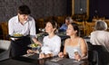 Young waiter serving dishes to female guests in restaurant Royalty Free Stock Photo