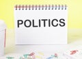 POLITICS the word is written on a blank sheet in a notebook standing on a table on a yellow background