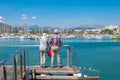 Couple of tourists on their backs, looking at the pier in the port of Pollensa on a sunny day