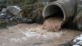 Polluted water flows from a large concrete pipe into a stream Royalty Free Stock Photo