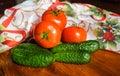 Red tomatoes and green cucumbers near a colorful tablecloth on a wooden board in the afternoon Royalty Free Stock Photo