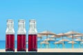 Pomegranate cold juice in bottles on the beach and straw umbrellas backgrounds