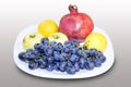 Pomegranate, grape with apple and lemon in a white plate