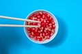 Pomegranate seeds with chopsticks in white bowl on a blue background