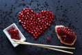 Pomegranate seeds are stacked in the form of a heart on a black background, next to a quarter of a pomegranate and Chinese chopsti Royalty Free Stock Photo