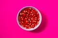 Pomegranate seeds in a white bowl on magenta background