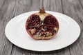 Pomegranates have broken into pieces with red berries on a porcelain plate on a dark background.