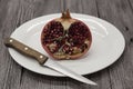 Pomegranates have broken into pieces with red berries on a porcelain plate with a knife on a dark background.