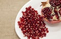 Pomegranates have broken into pieces with red berries on a porcelain plate on a textile background.