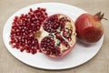 Pomegranates have broken into pieces with red berries on a porcelain plate on a textile background.