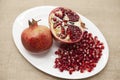 Pomegranates have broken into pieces with red berries on a porcelain plate on a textile background.