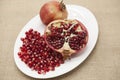 Pomegranates have broken into pieces with red berries on a porcelain plate on a textile background.