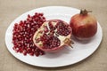 Pomegranates have broken into pieces with red berries on a porcelain plate on a textile background.