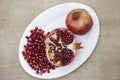 Pomegranates have broken into pieces with red berries on a porcelain plate on a textile background.