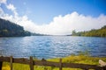 Pond isolated with a wooden fence, green grass around, cloudy blue sky background Royalty Free Stock Photo