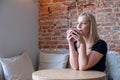 Pondering attractive blonde young woman with coffee in hand thinking on plans enjoying recreation time in stylish Royalty Free Stock Photo