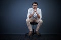 In a ponderous mood. Studio portrait of a handsome young businessman sitting on a chair against a dark background.