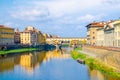 Ponte Vecchio bridge with colourful buildings houses over Arno River blue reflecting water and boats near river bank in Florence