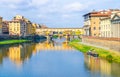Ponte Vecchio bridge with colourful buildings houses over Arno River blue reflecting water and boats near river bank in Florence