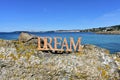 Coast with Dream wooden sign on the rocks. Blue sea, sunny day. Rias Baixas, Spain.