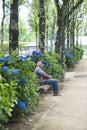 An elderly man rests, sitting on a wooden bench